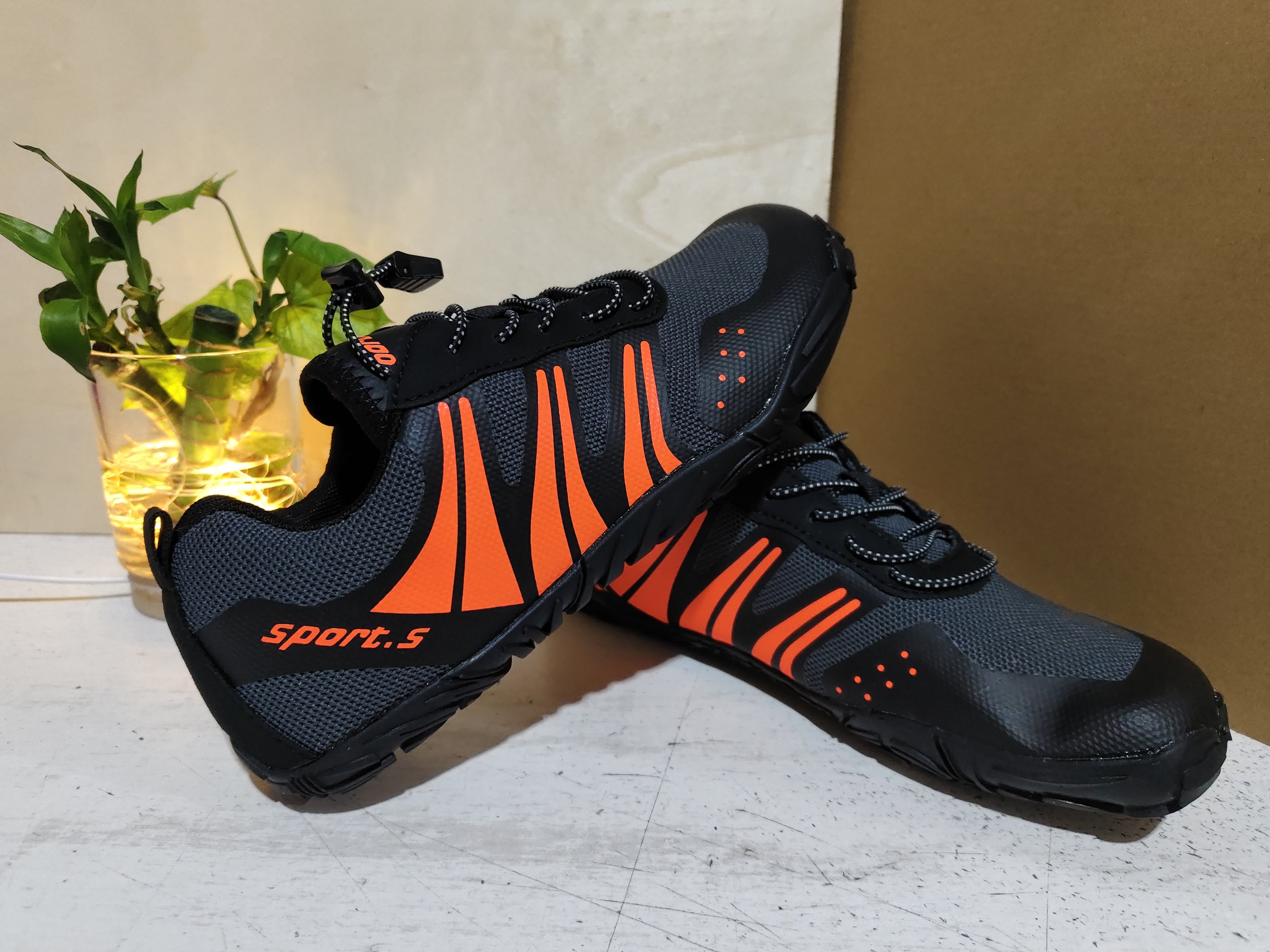 Black and orange Outdoor Wading Shoes, Quick-drying Shoes, Beach Shoes, Hiking Shoes, Fishing Sports Shoes with a sporty design displayed on a white surface with a small green plant in the background.