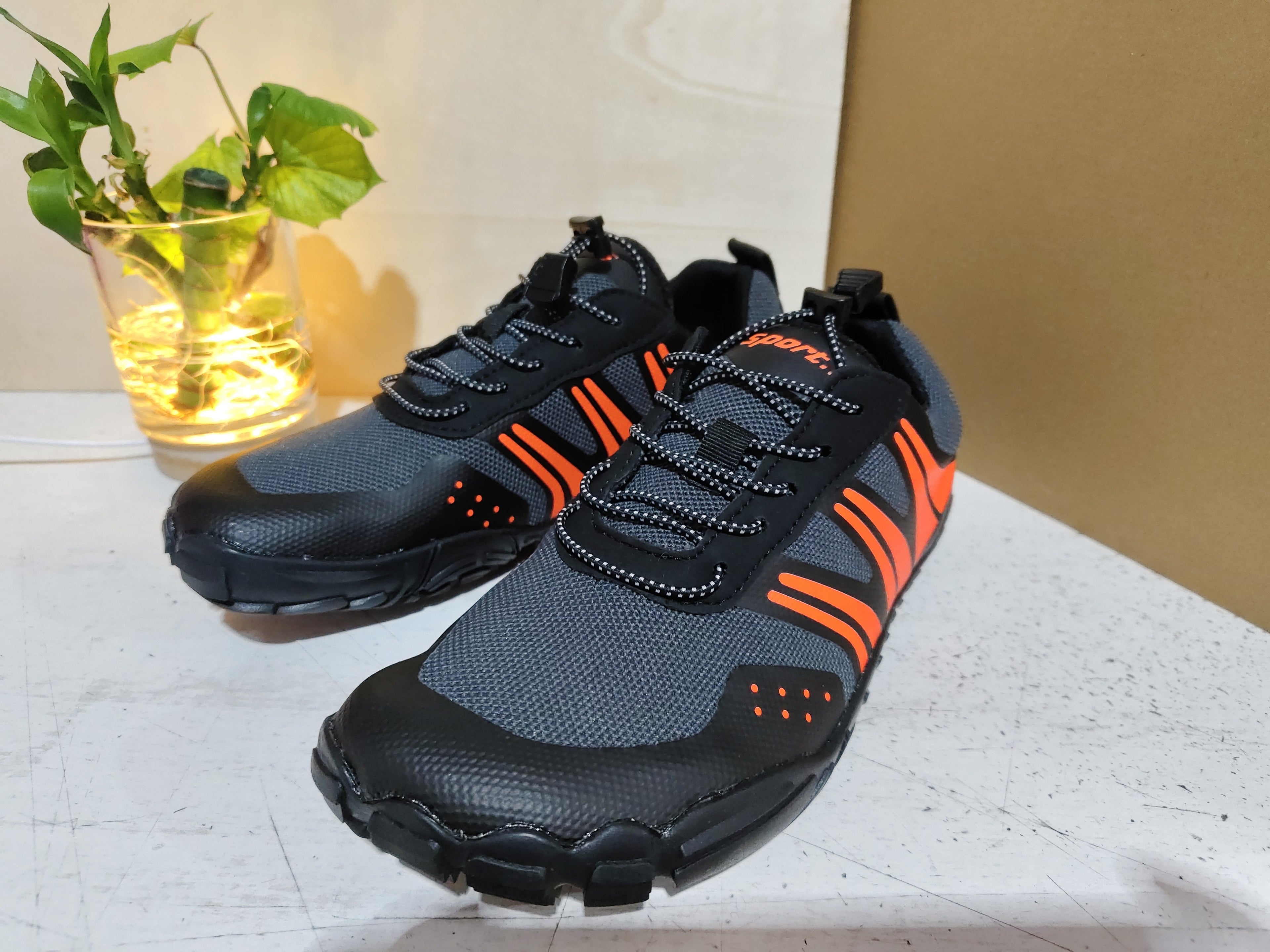 Pair of black and gray Outdoor Wading Shoes, Quick-drying Shoes, Beach Shoes, Hiking Shoes, Fishing Sports Shoes with orange accents on a white surface next to a small potted plant.